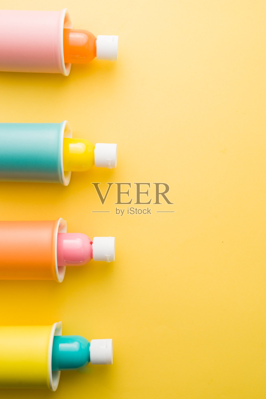 瓶子里面充满了绘画颜色的不同颜色的苗条马克杯，吸引构图在黄色的背景照片摄影图片