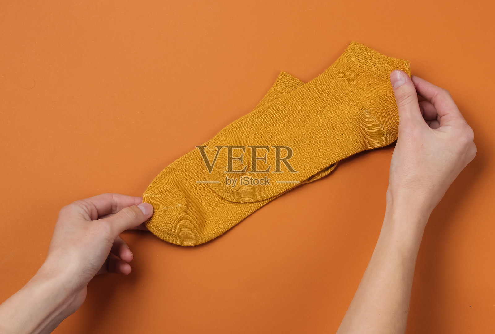 女人手持橙色袜子，棕色背景，俯视照片摄影图片