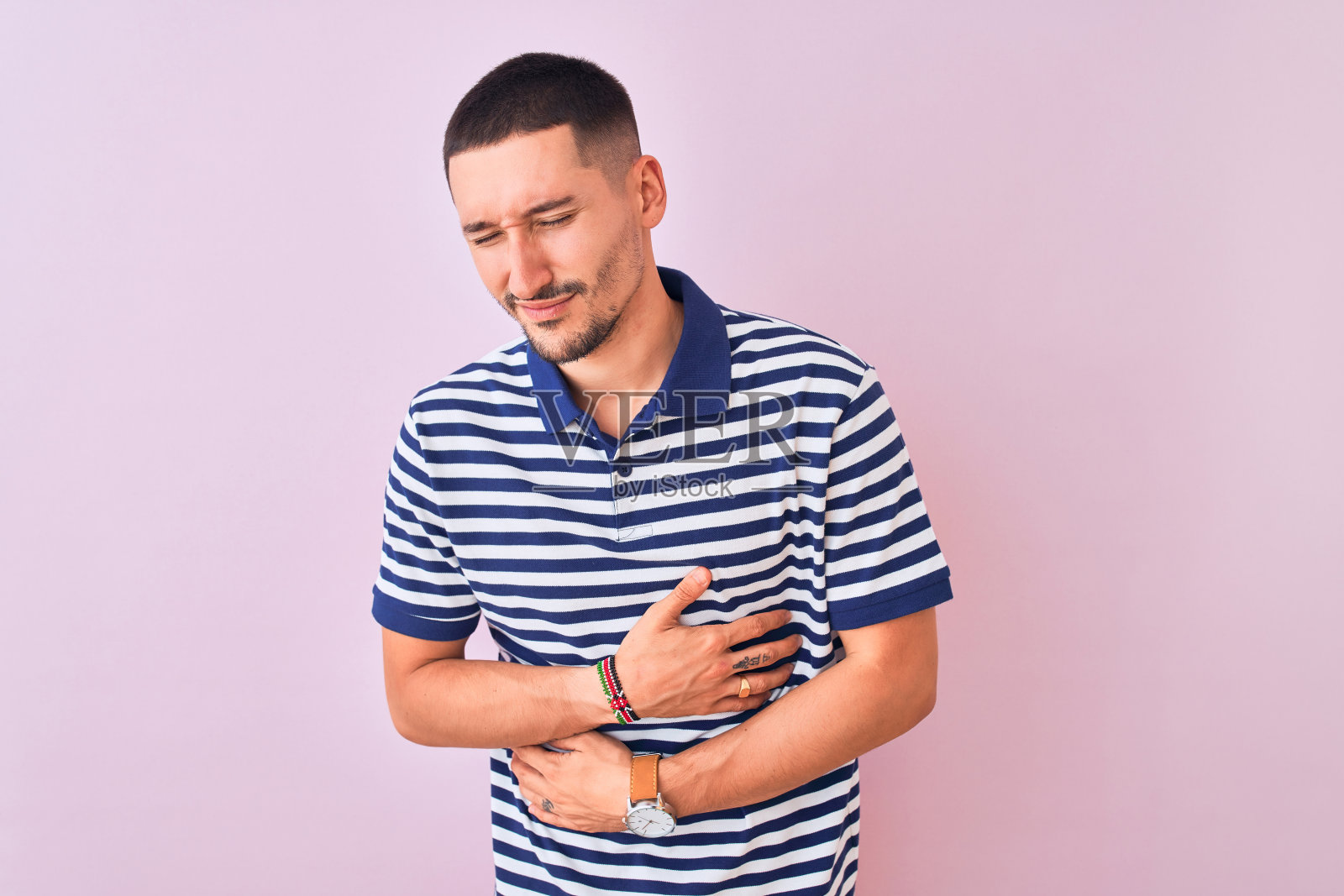 年轻帅气的男子穿着航海条纹t恤在粉红色孤立的背景与手胃，因为恶心，痛苦的疾病感觉不舒服。疼痛的概念。照片摄影图片