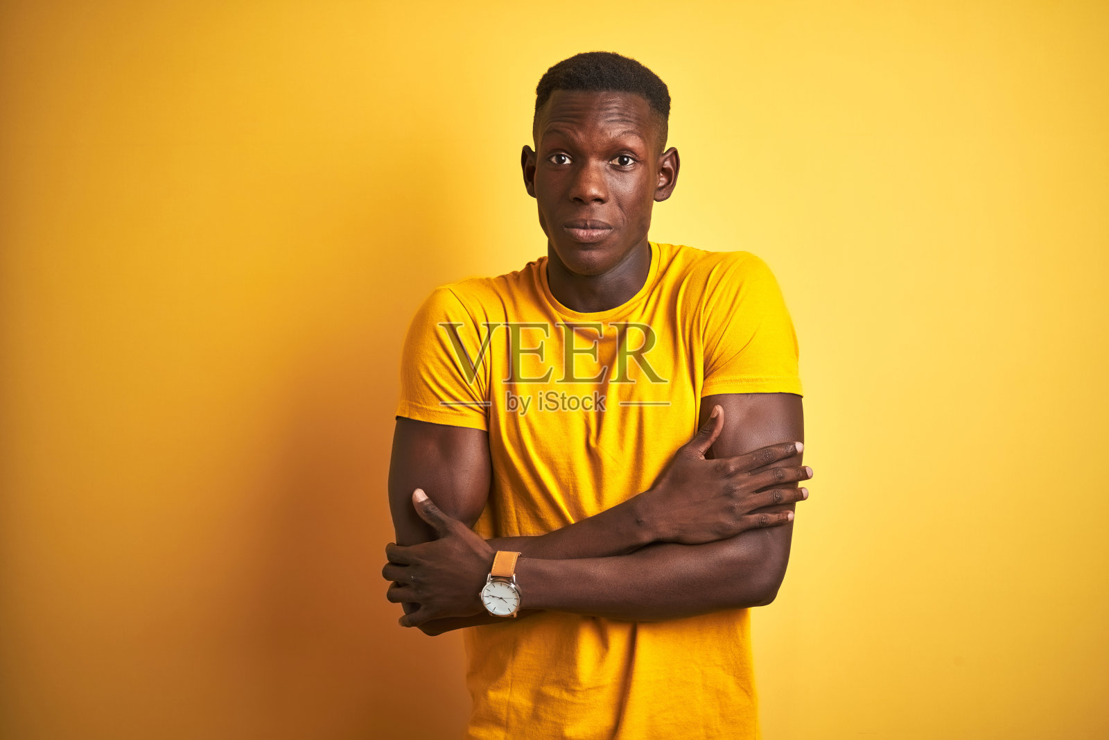 年轻的非裔美国男子身穿休闲T恤，站在孤立的黄色背景上，因冬天的寒冷而颤抖和冻结，脸上带着悲伤和震惊的表情照片摄影图片