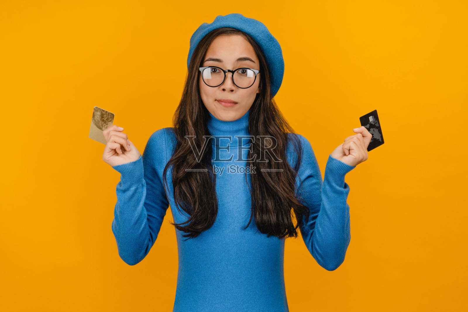 年轻漂亮的女商人摆出孤立的黄色背景持有两张信用卡选择照片摄影图片