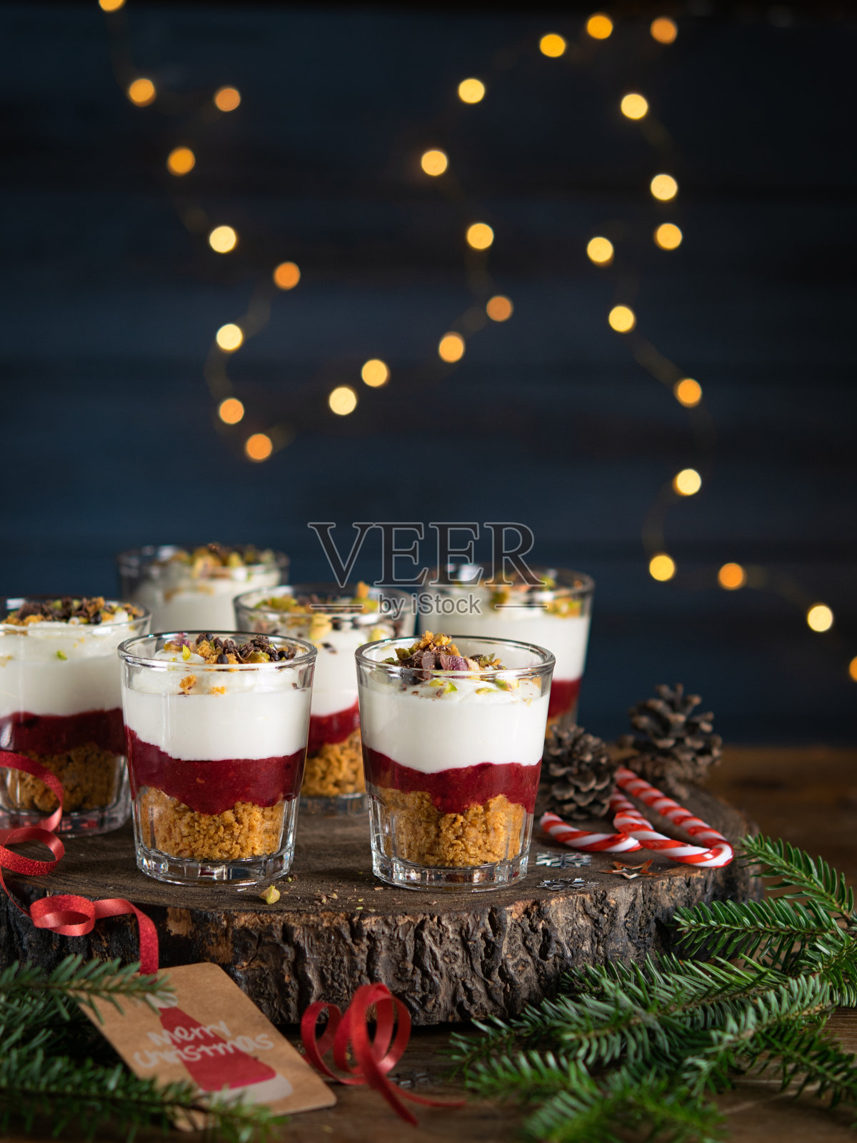 甜点在玻璃杯中与巧克力和浆果铺在木制的背景，花环灯散焦和圣诞装饰。圣诞、新年假日背景概念。甜点食谱的想法。照片摄影图片