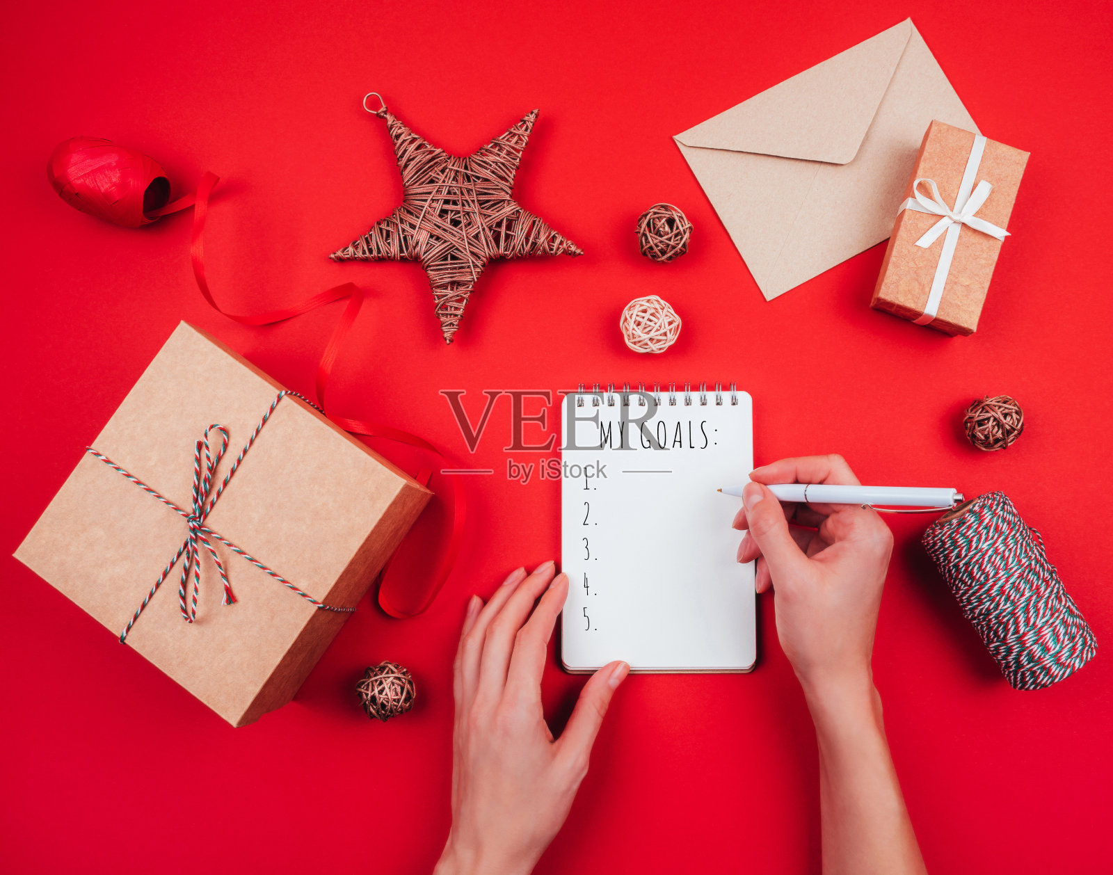 红色节日背景上的空白笔记本、笔、工艺礼品盒、信封、红色蝴蝶结、三色绳线和装饰品。新年计划。照片摄影图片