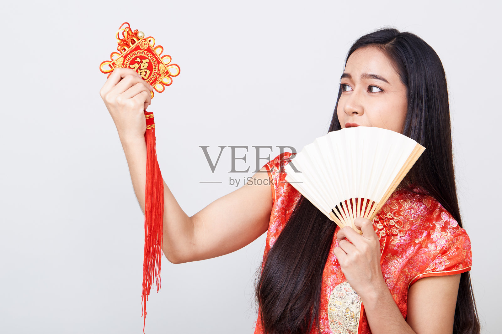 年轻女子身着旗袍，手持带有中国传统装饰的扇子，对着镜头微笑，意味着好运照片摄影图片