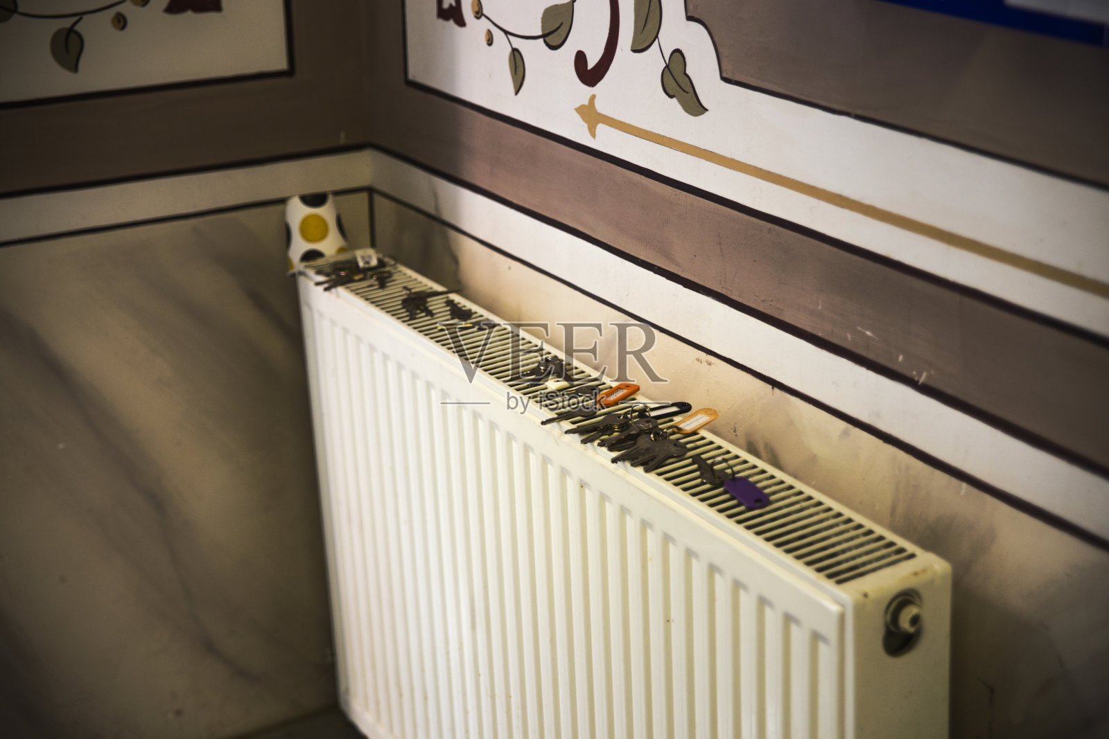 许多门的钥匙留在一个现代散热器加热器上，在一个古典的室内墙壁刺绣。照片摄影图片