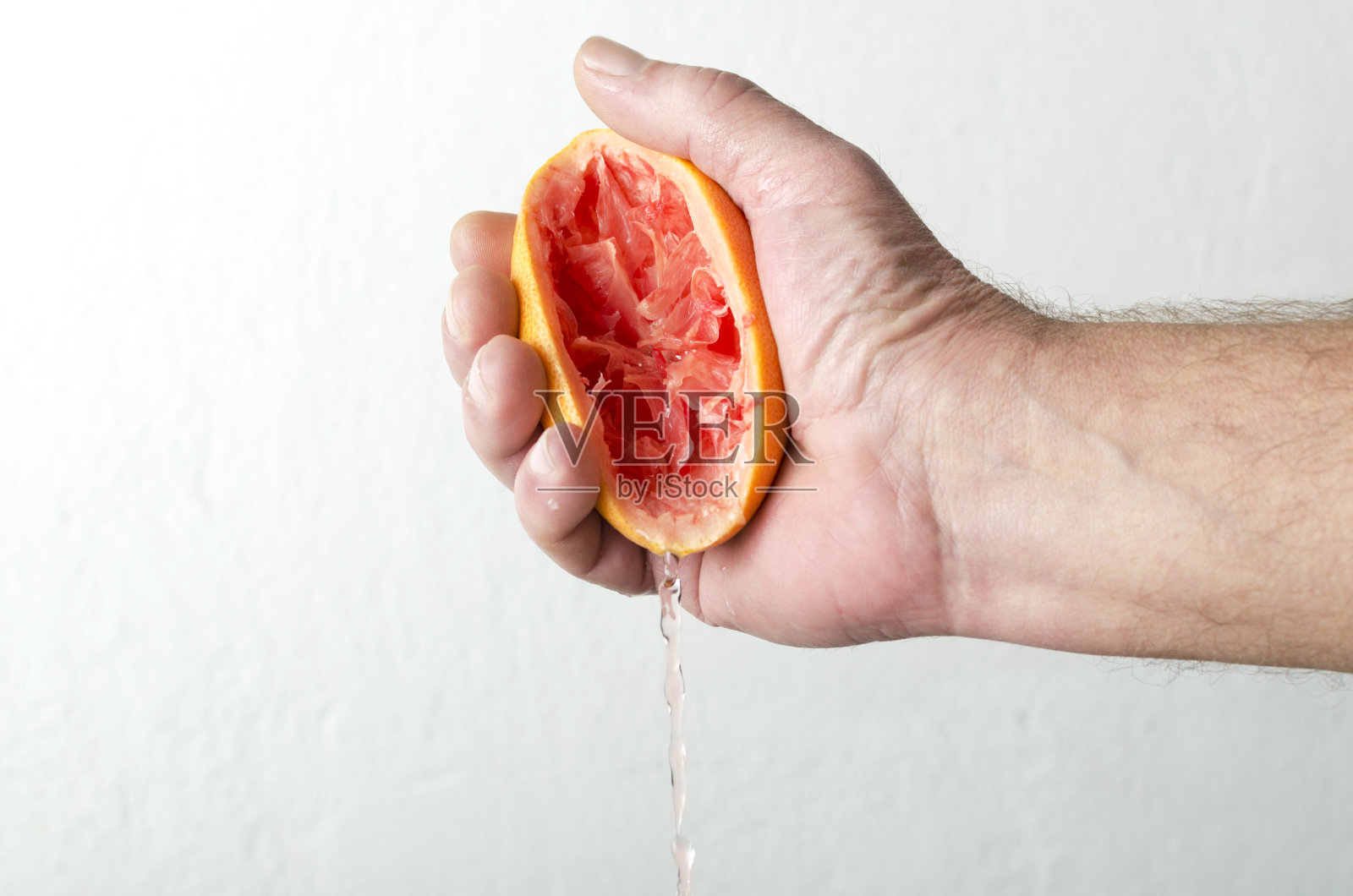 男人挤压葡萄柚汁，手中拿着挤压的葡萄柚靠在白墙上照片摄影图片