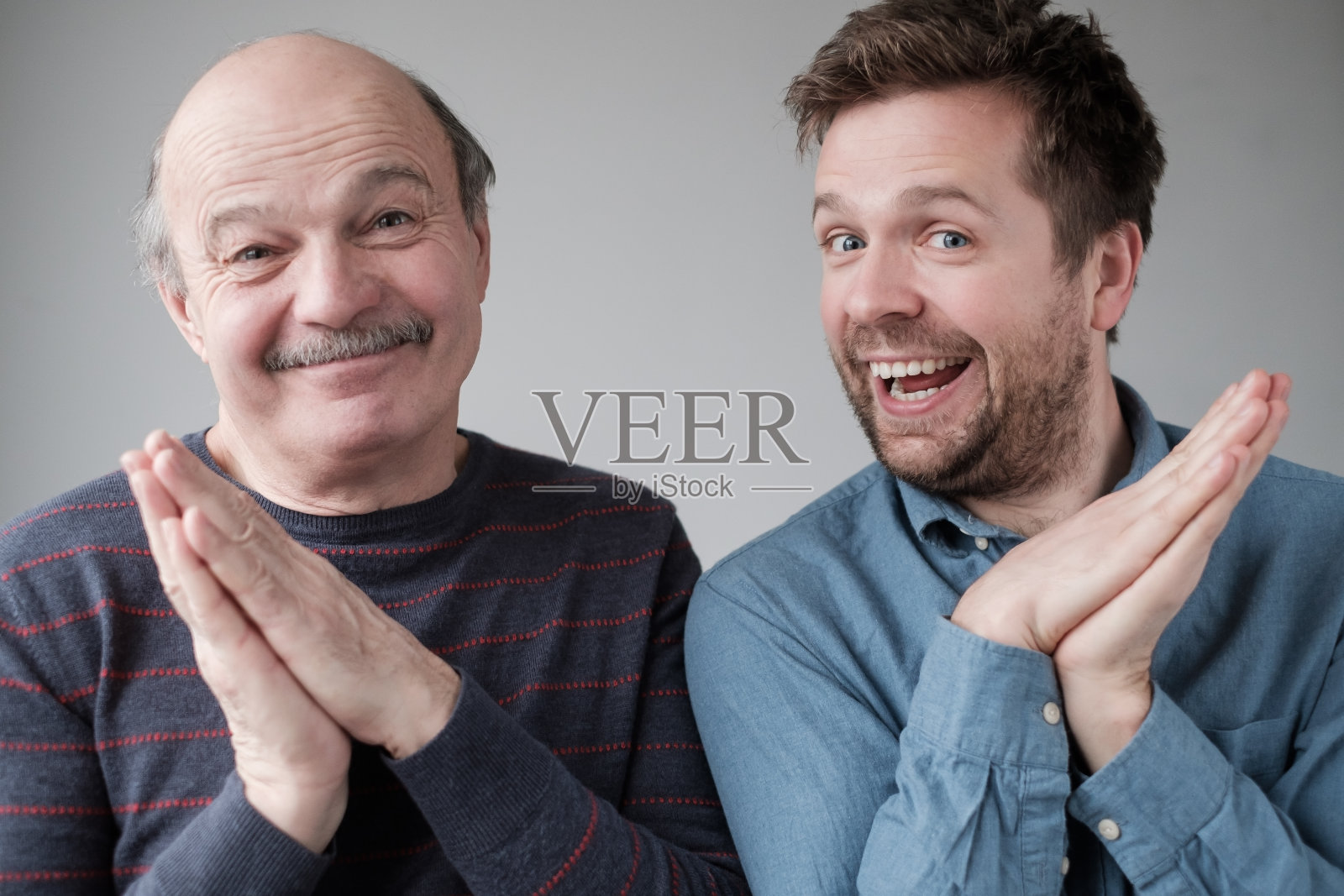 成熟的父子俩神秘地微笑着，紧握着双手，盘算着什么，保守着秘密照片摄影图片