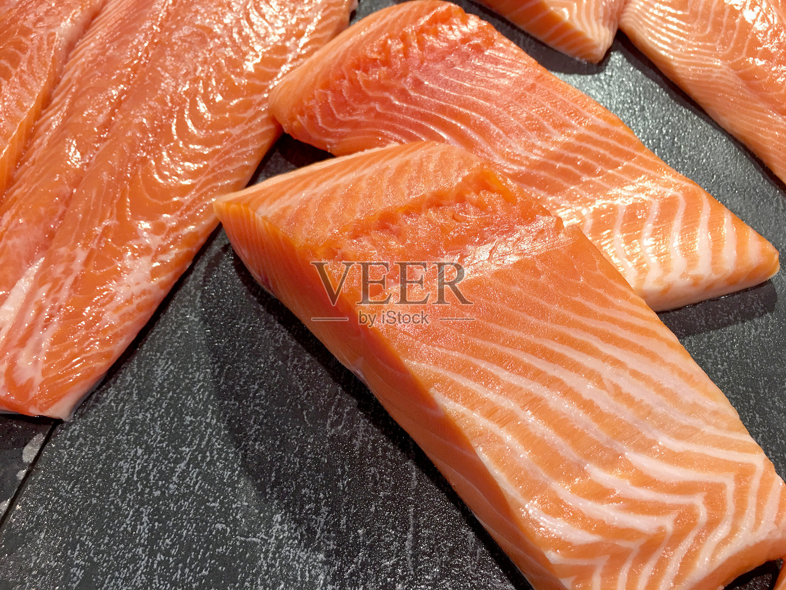 切片生鲑鱼或新鲜鲑鱼。在市场上出售的三文鱼片，以拼接的效果展示。许多新鲜的三文鱼肉片在一个黑色的托盘在超市出售。照片摄影图片