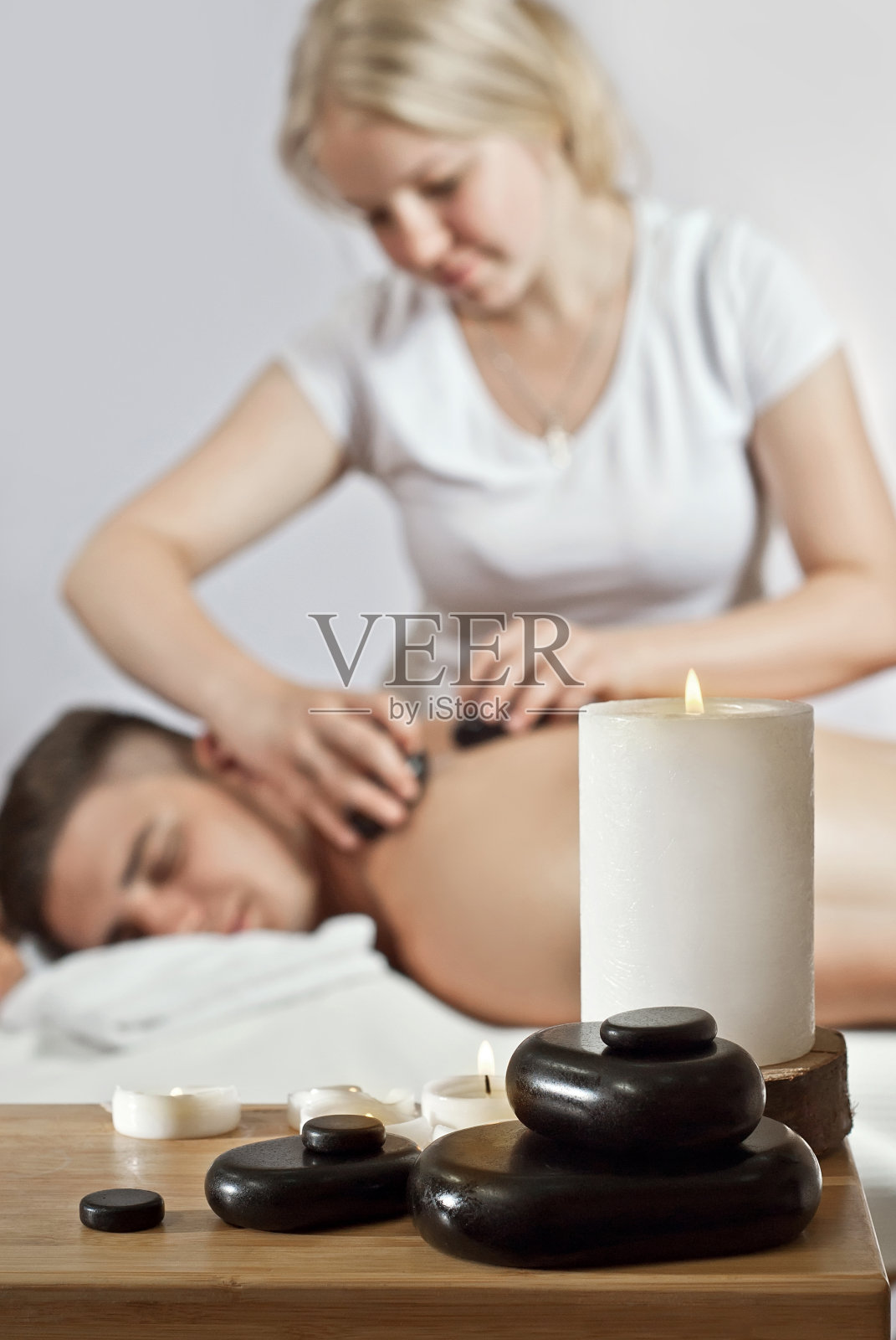 穿着白色T恤的按摩理疗师正在进行背部按摩，顾客面朝下躺在按摩床上照片摄影图片