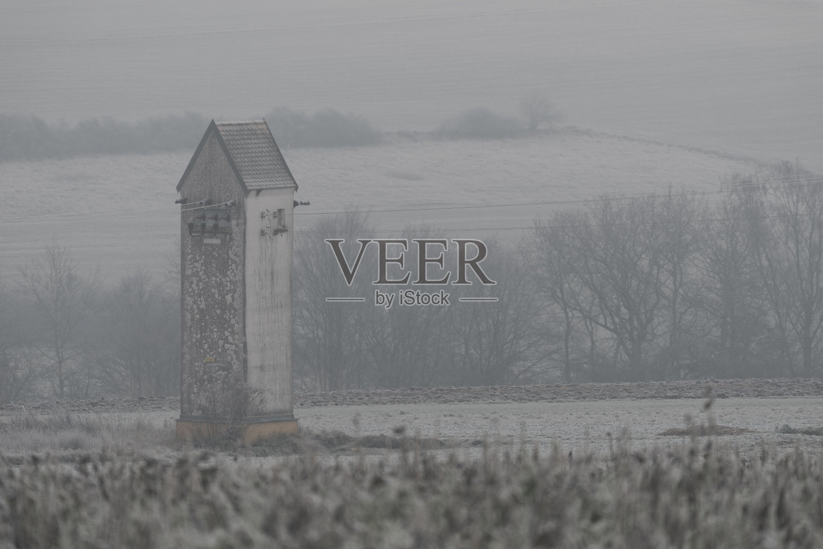 在冬天大雾弥漫的早晨，旧的变电站在白雪覆盖的田野里照片摄影图片