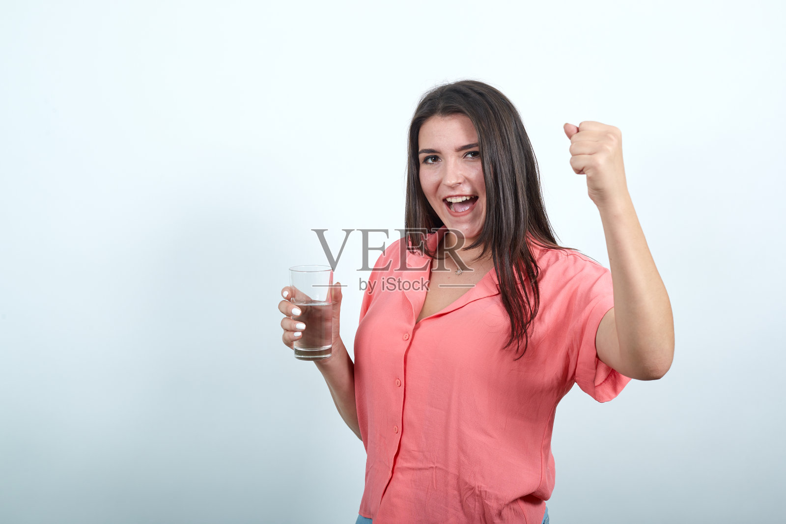 漂亮女人拿着一杯水，用拳头做胜利者的手势照片摄影图片