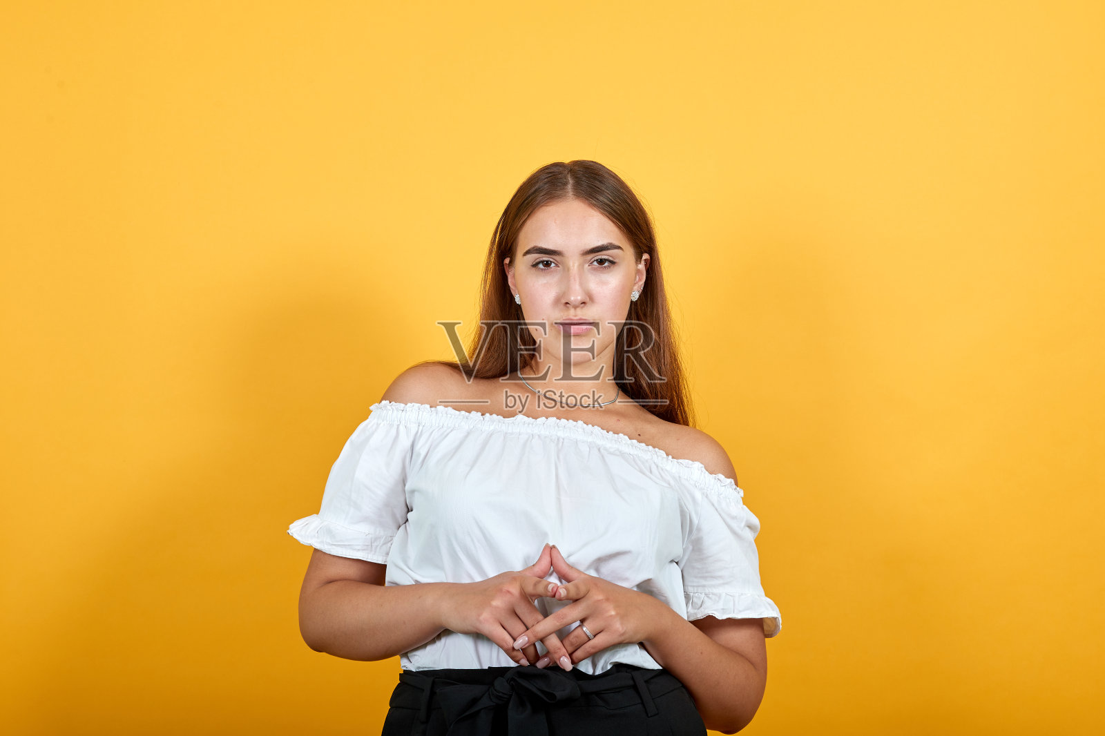 严厉的年轻女子手牵着手，看着镜头，严肃的女孩照片摄影图片