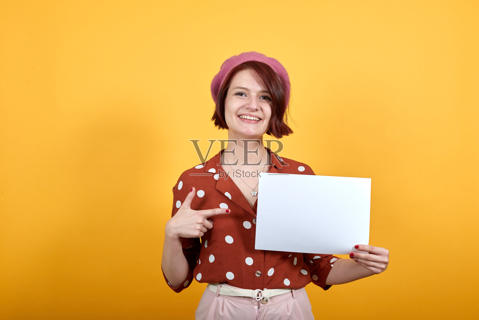 漂亮的白人年轻女子拿着空白的白纸，用手指着照片摄影图片