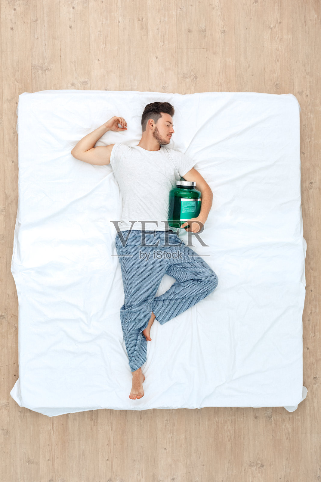 睡觉前。一个人放松地睡在床上俯视图与健美补充剂显示二头肌照片摄影图片