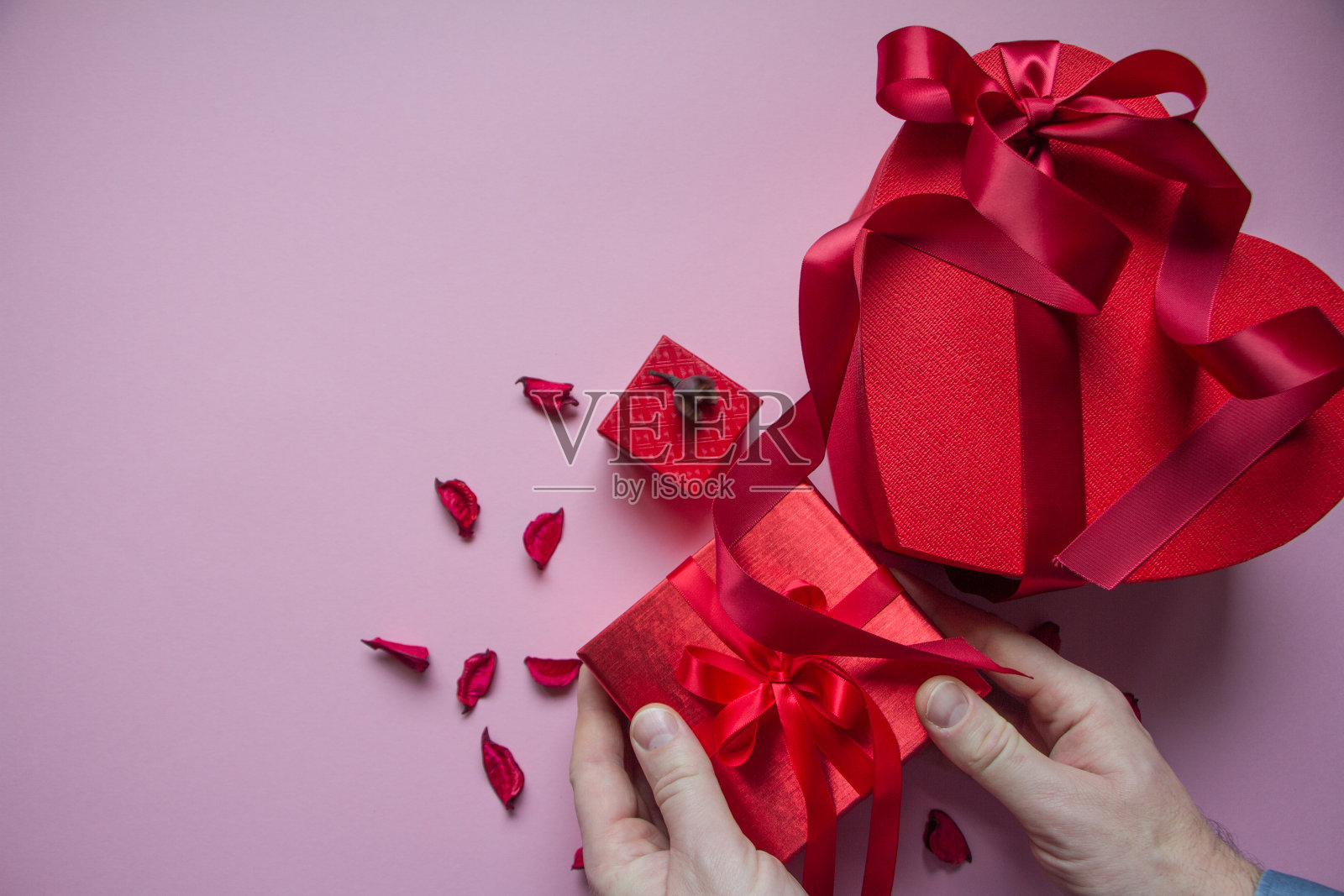男人用红色丝带包裹粉色背景下的红色心形礼品盒，礼品概念照片摄影图片