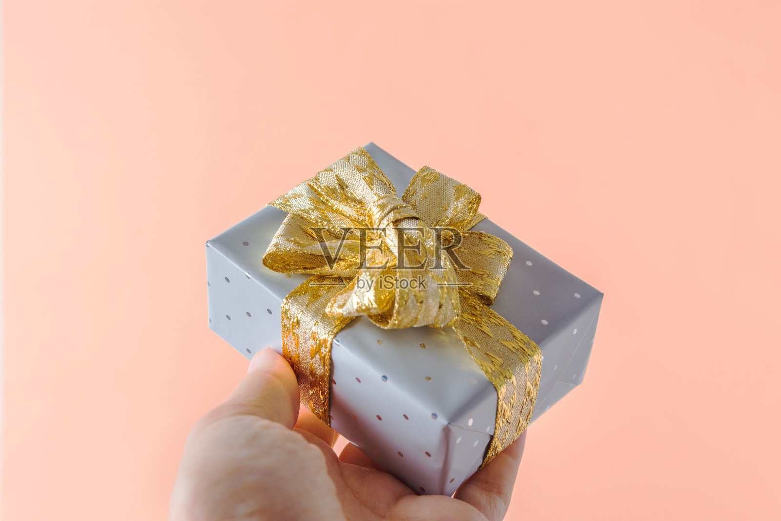 年轻的白人妇女手里拿着礼品盒包装在银色的纸与金色丝带蝴蝶结在粉红色的背景。圣诞新年情人礼物照片摄影图片