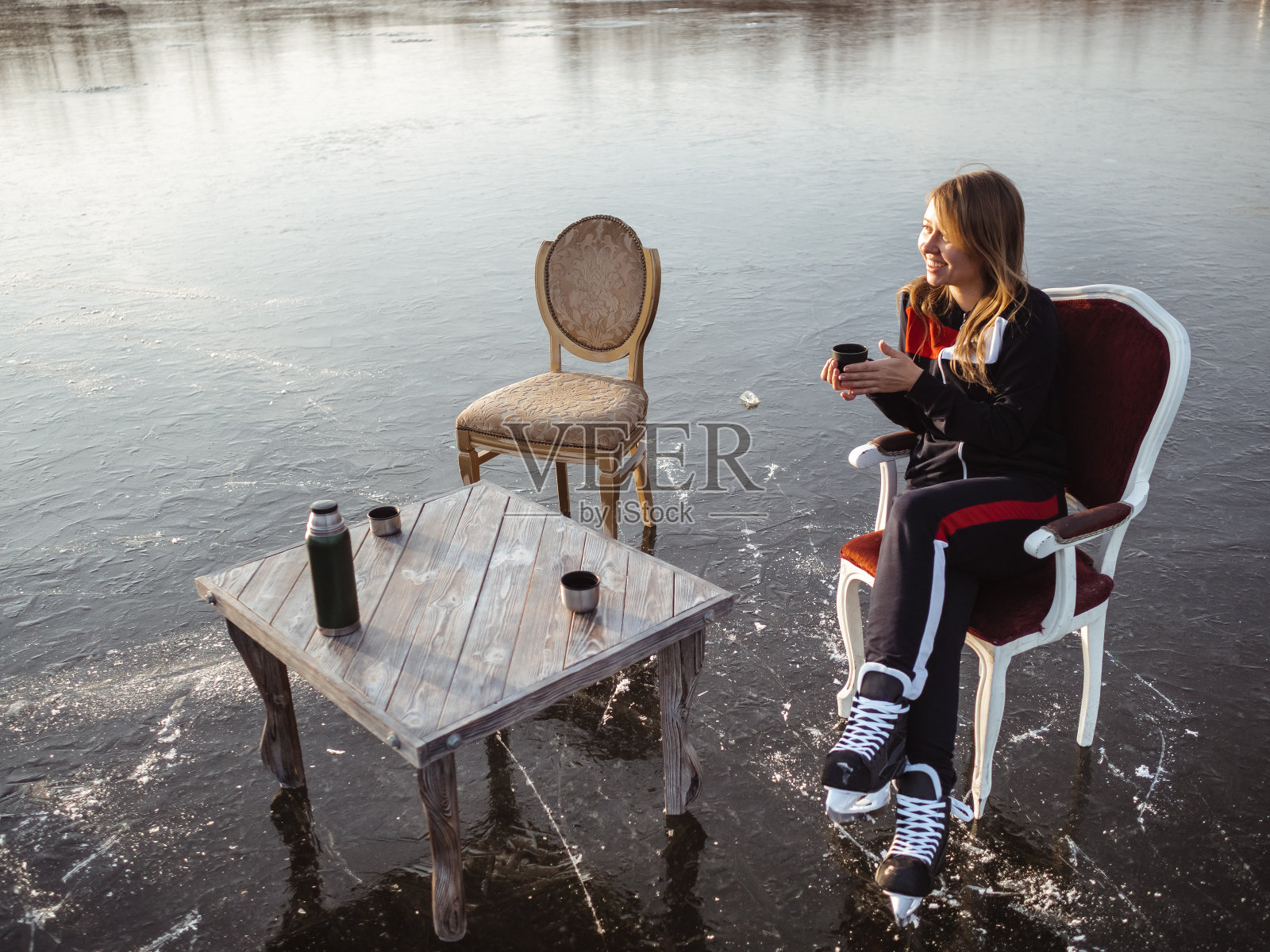 一个穿着冰鞋的女孩坐在森林里结冰的湖面上的桌子旁。热水瓶茶照片摄影图片