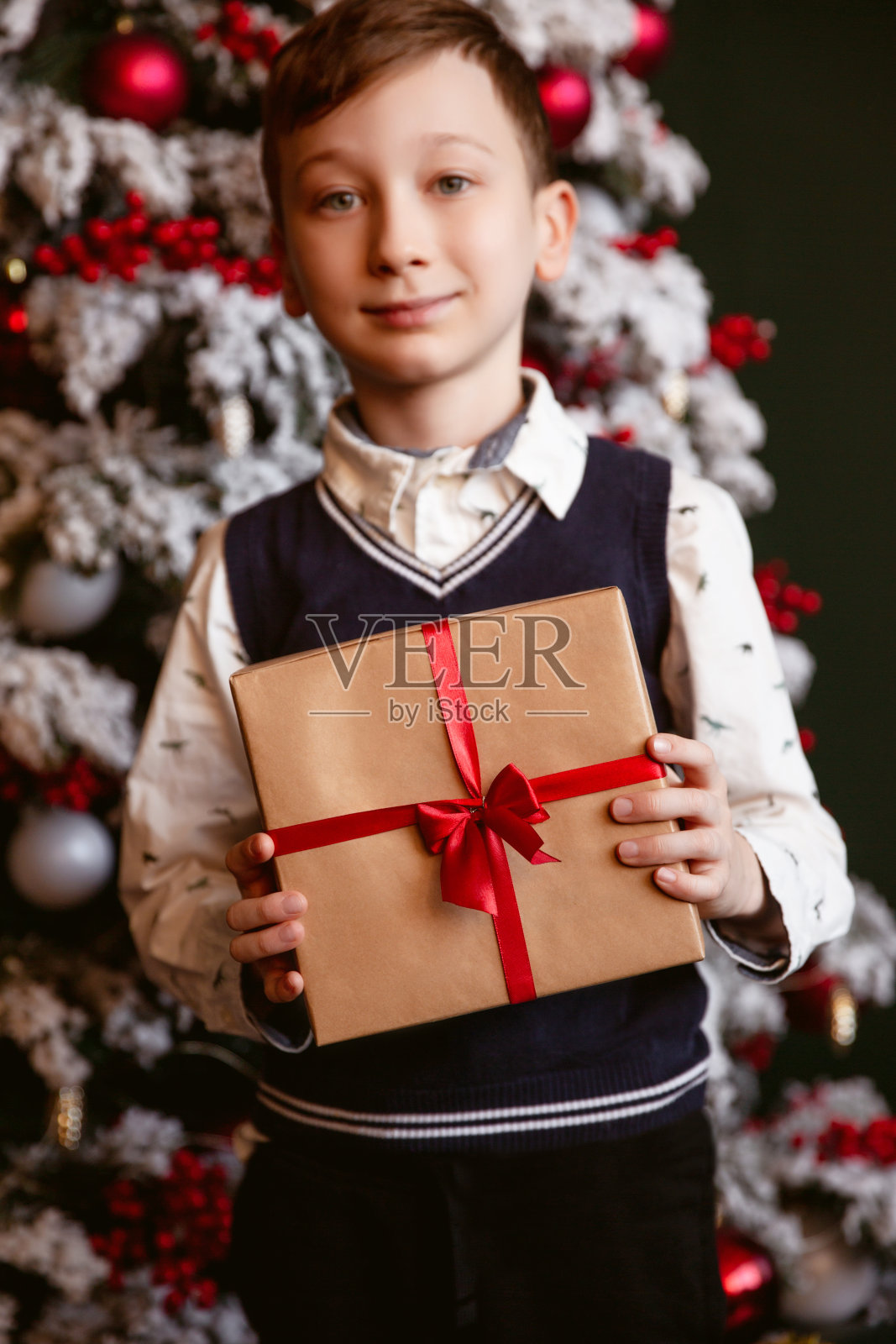 男孩拿着圣诞礼物在圣诞树的背景。寒假的概念。照片摄影图片