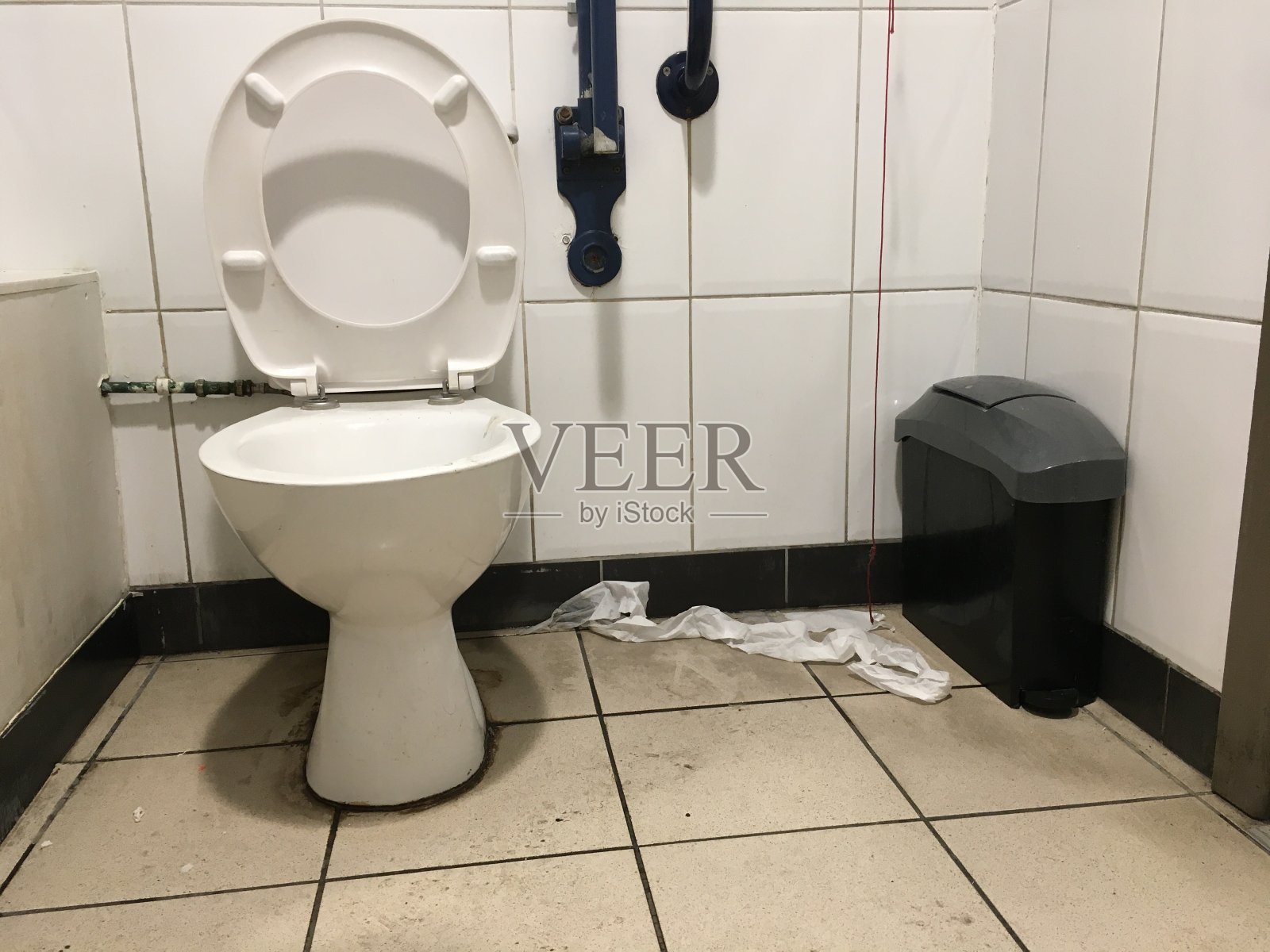 肮脏的厕所隔间，厕纸留在肮脏的瓷砖地板上照片摄影图片