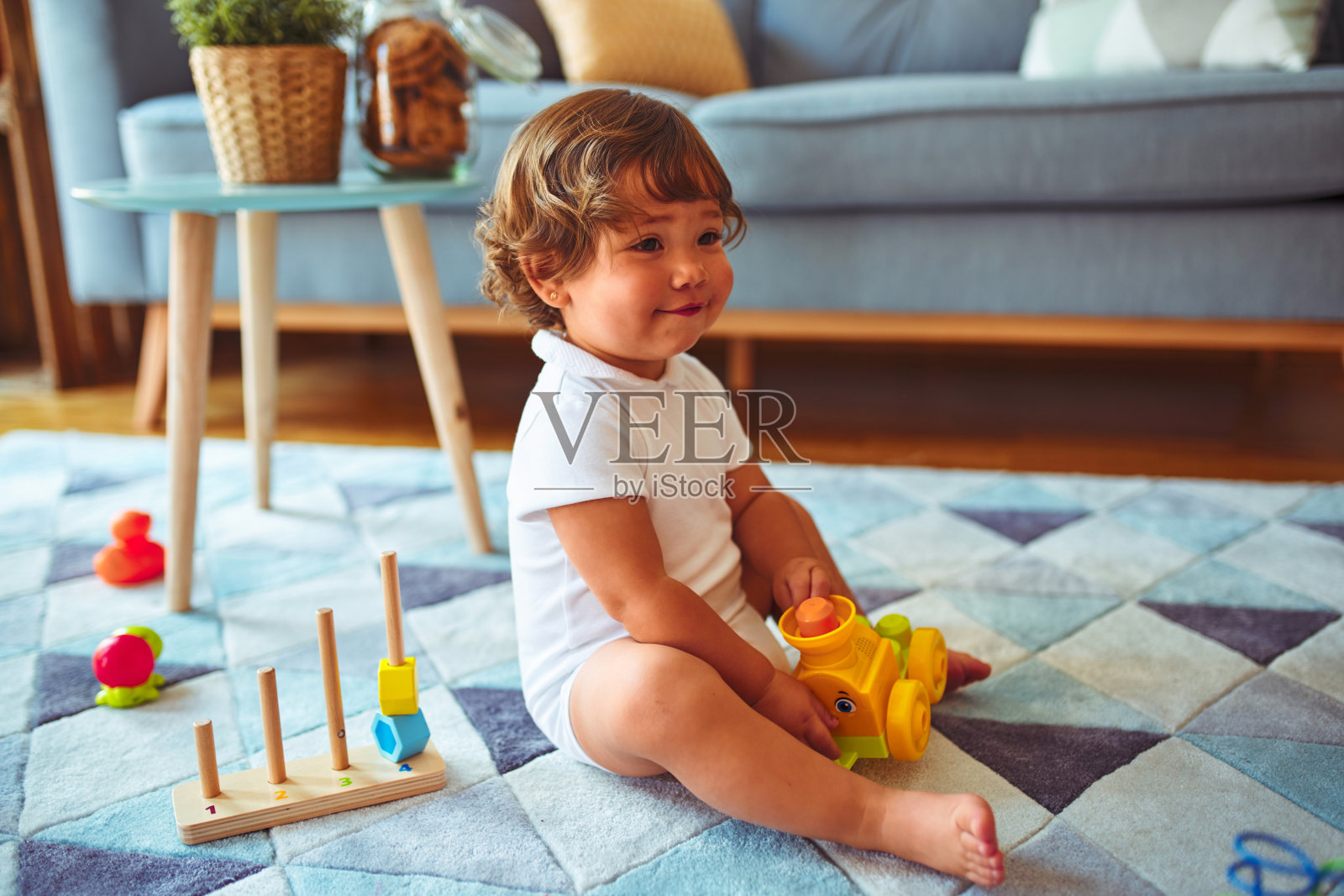 漂亮的蹒跚学步的小女孩在地毯上玩玩具照片摄影图片