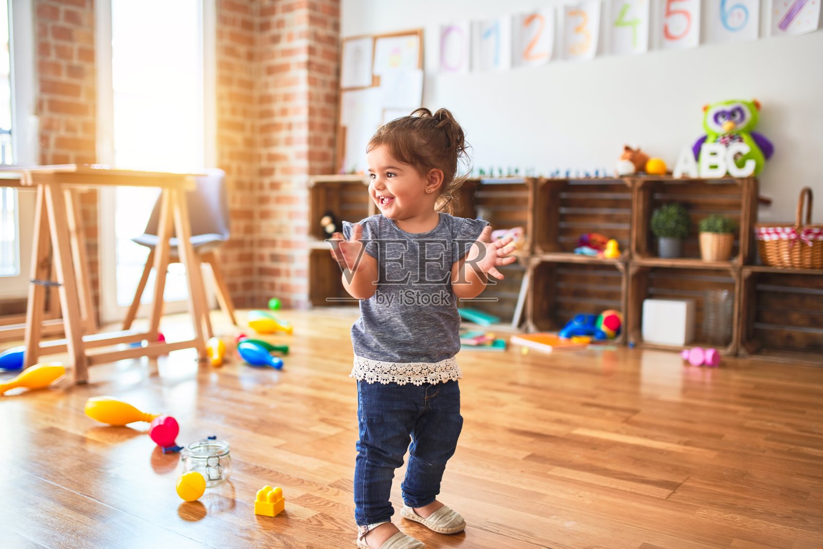 在幼儿园里，美丽的幼童站在一堆玩具周围鼓掌照片摄影图片