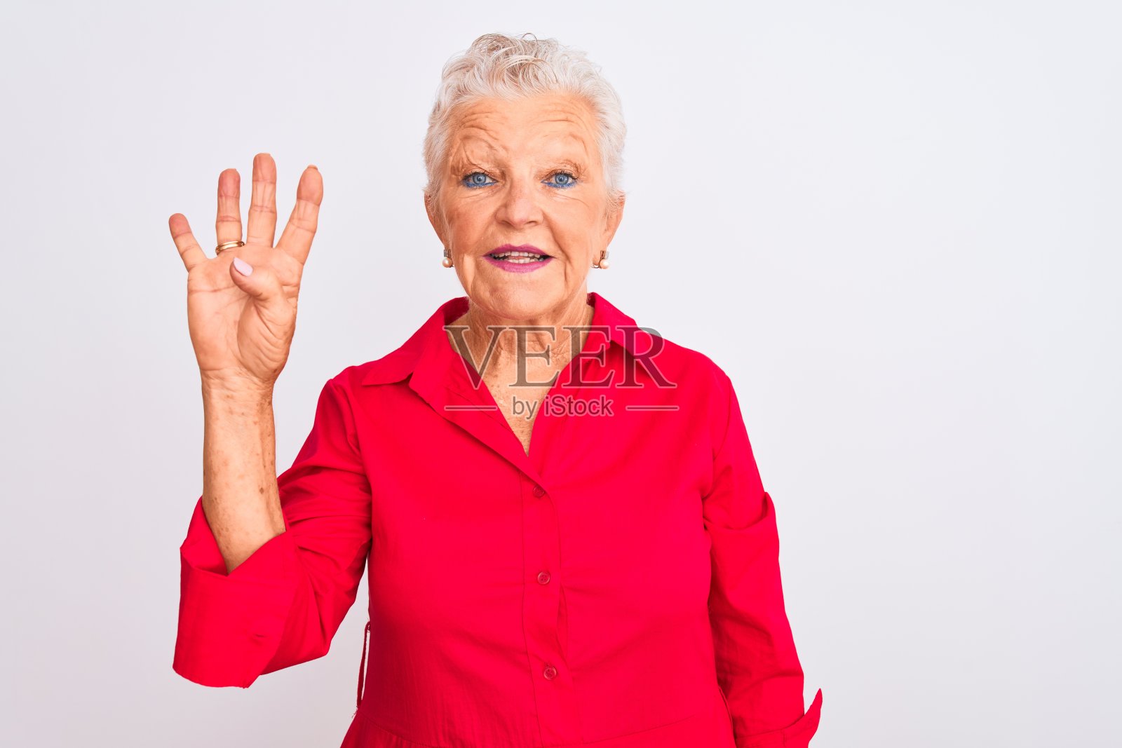 一位灰白头发的老妇人穿着红色休闲衬衫，站在孤立的白色背景下，用第四个手指指着上面，同时微笑着，自信而快乐。照片摄影图片
