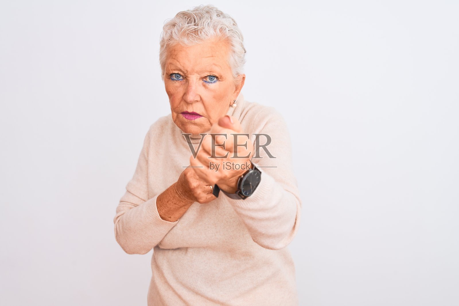 年长的白发女子穿着高领毛衣站在孤立的白色背景上，准备用拳头打拳的姿势，一脸愤怒和不安，怕出问题照片摄影图片