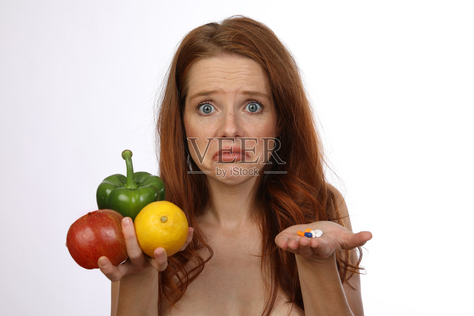 一位红头发的年轻女子把水果、蔬菜和药片放在面前，还没有决定照片摄影图片