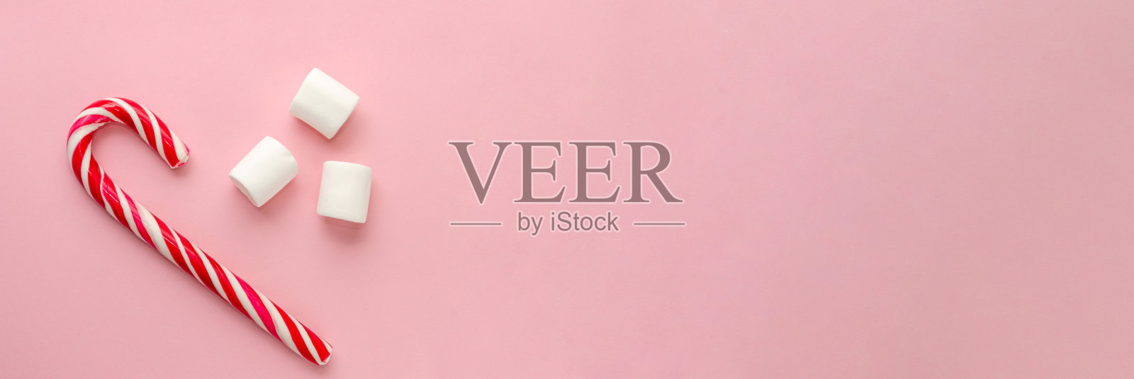 拐杖糖和三个白色棉花糖在千禧粉背景上。横幅。圣诞最小平铺。本空间照片摄影图片