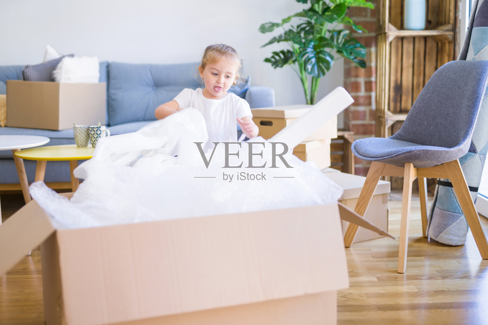 漂亮的蹒跚学步的小女孩在新家玩盒子照片摄影图片