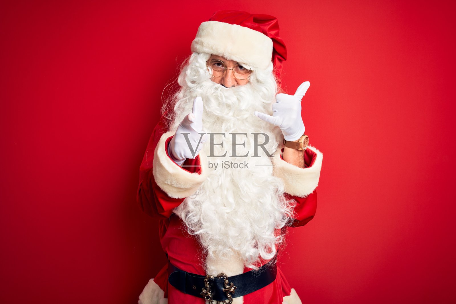中年英俊的男人穿着圣诞老人服装站在孤立的红色背景微笑做电话交谈手势和指向你。打电话给我。照片摄影图片