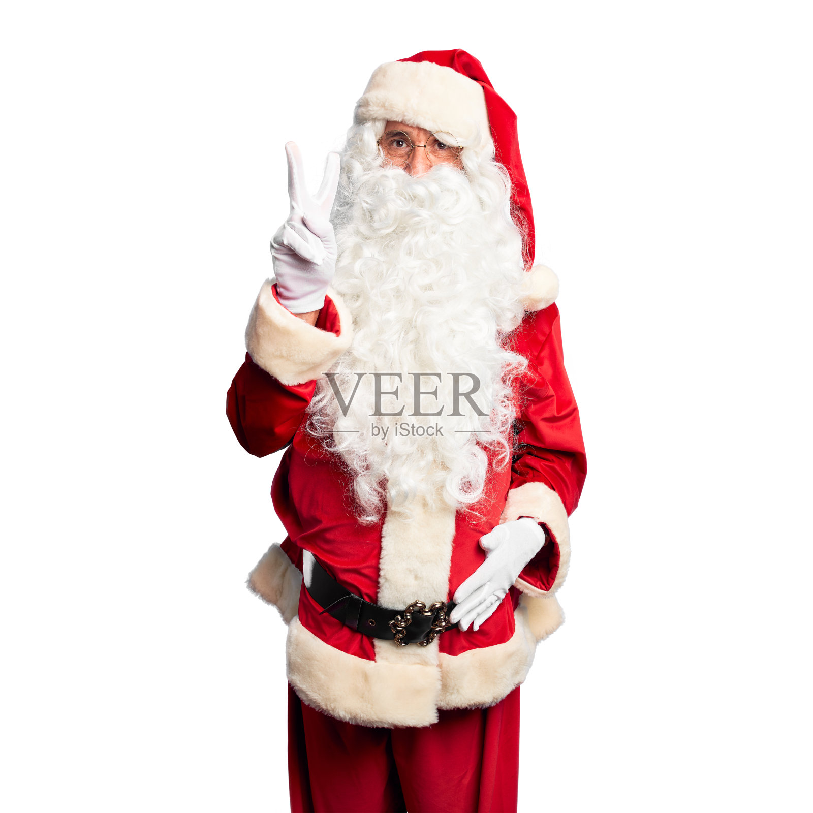 英俊的中年男子穿着圣诞老人的服装和胡子站在展示和指向第二手指，同时自信和快乐的微笑。照片摄影图片