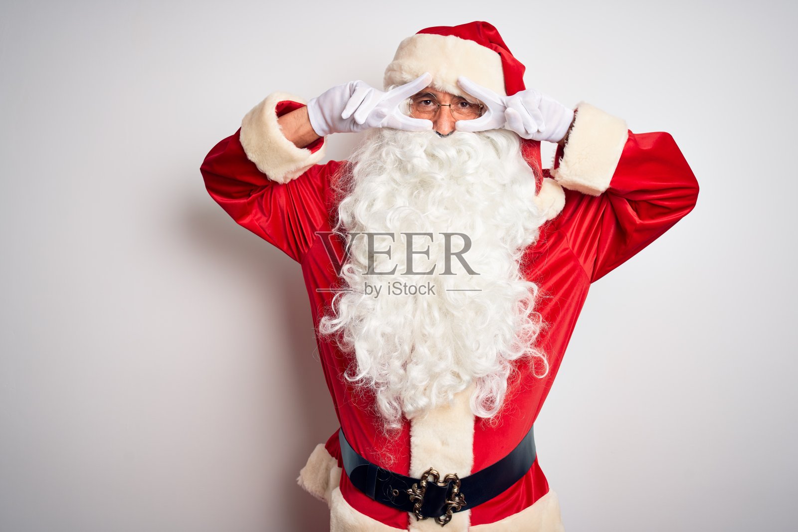 穿着圣诞老人服装的中年英俊男子站在孤立的白色背景做和平的象征，手指在脸上，微笑着，欢快地显示胜利照片摄影图片