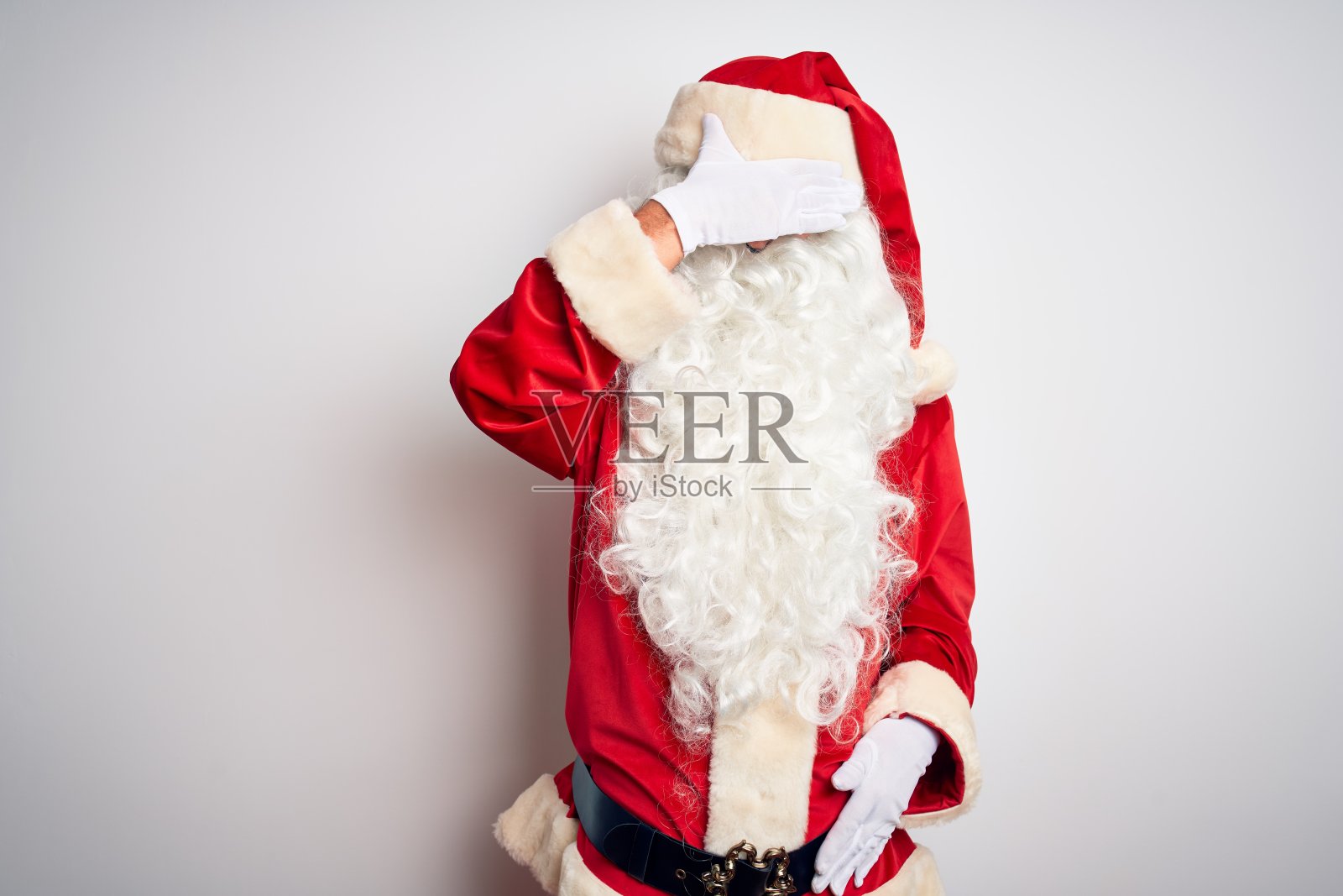 中年英俊的男人穿着圣诞老人的服装站在孤立的白色背景用手遮住眼睛，看起来严肃和悲伤。失明，隐藏和排斥的概念照片摄影图片