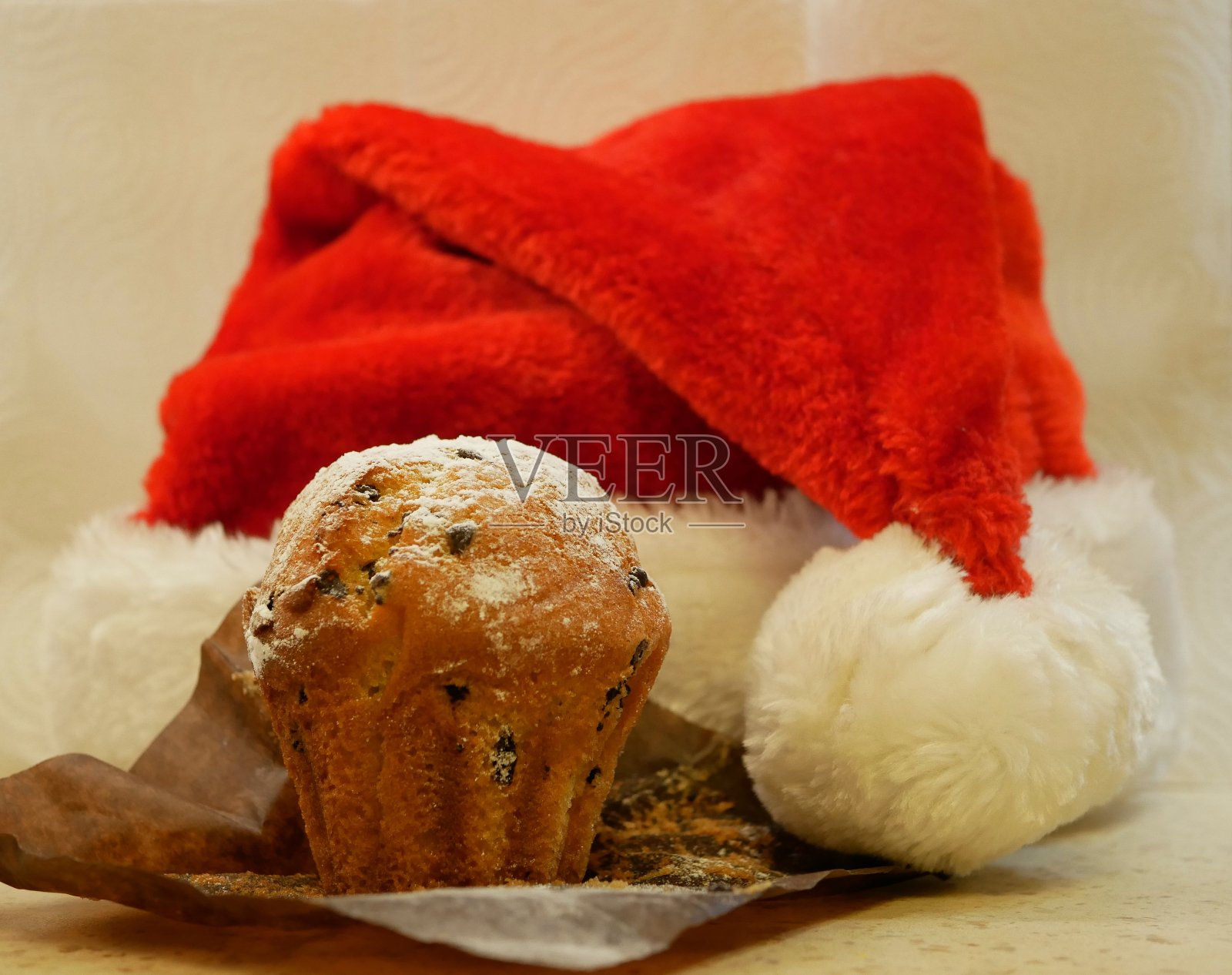 一个巧克力松饼，撒上糖粉当雪，背景是新年的红帽和白色的绒球，营造节日气氛。照片摄影图片