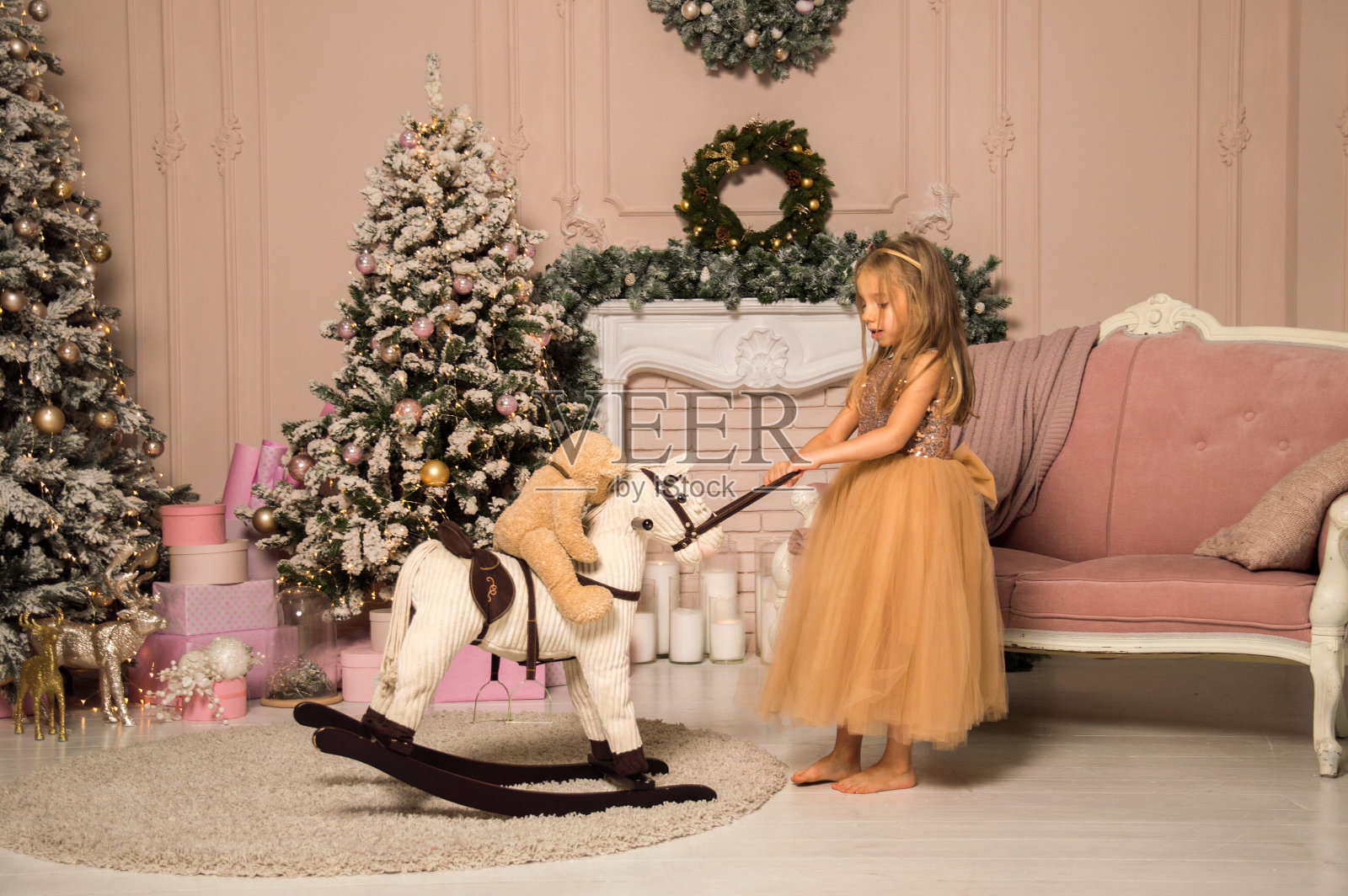 关闭了。一个小女孩用皮带拉着马鞍上有一只熊的玩具木马。用圣诞树装饰的节日的房间。照片摄影图片