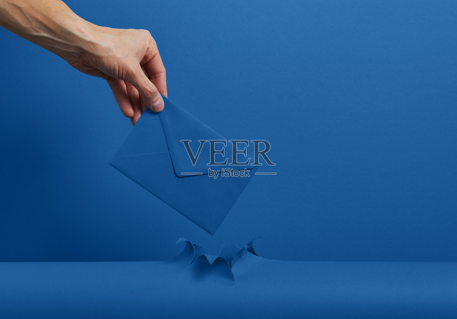 男手拿着一个信封，里面有一封穿过撕烂的经典蓝色纸背景的信。好消息和礼物的概念。照片摄影图片