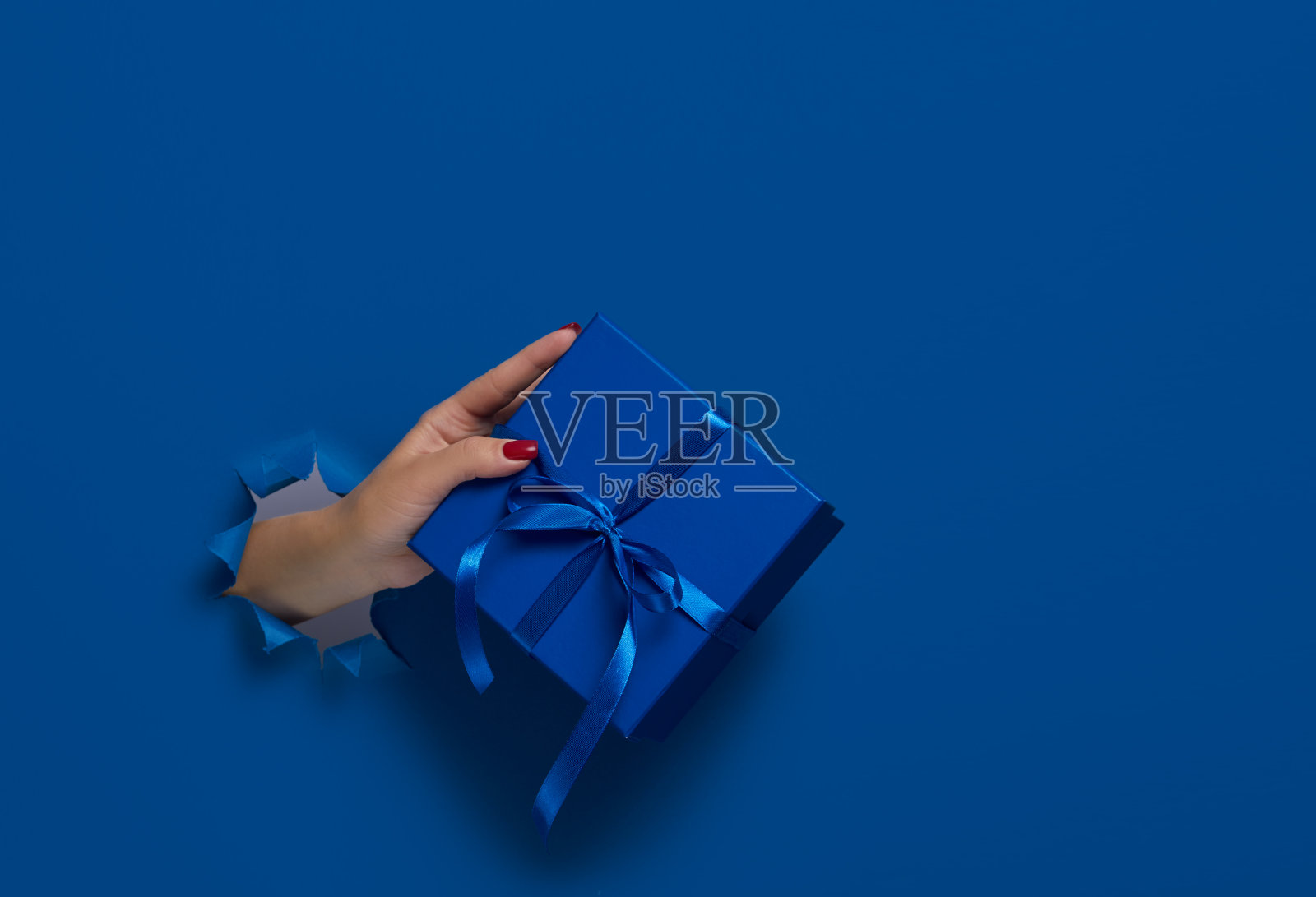 特写的女性手拿着礼物盒通过一个撕裂的深蓝色的纸，模型。文本复制空间照片摄影图片