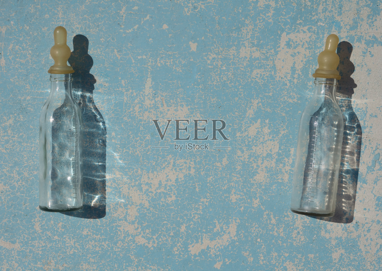 空的透明婴儿奶瓶喂养新生儿与阴影在蓝色柔和的颜色木质背景下，在自然的阳光下。平的。照片摄影图片