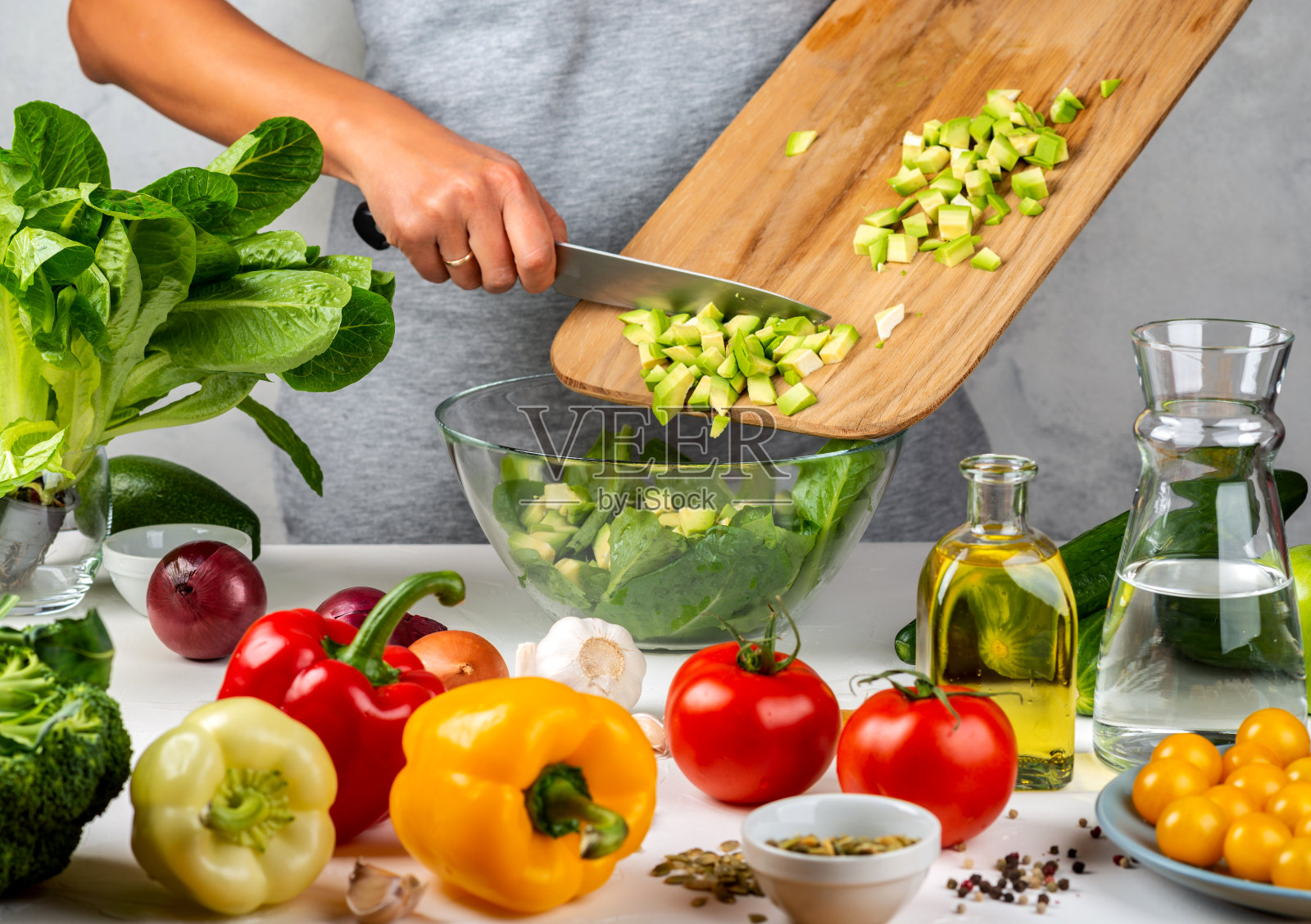 在厨房里，一名女子正在往一个玻璃碗里的沙拉里加碎牛油果。健康饮食的概念。照片摄影图片