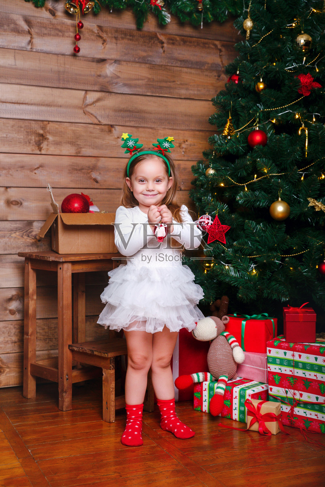 美丽快乐的小女孩带着圣诞球在家里的圣诞树旁照片摄影图片