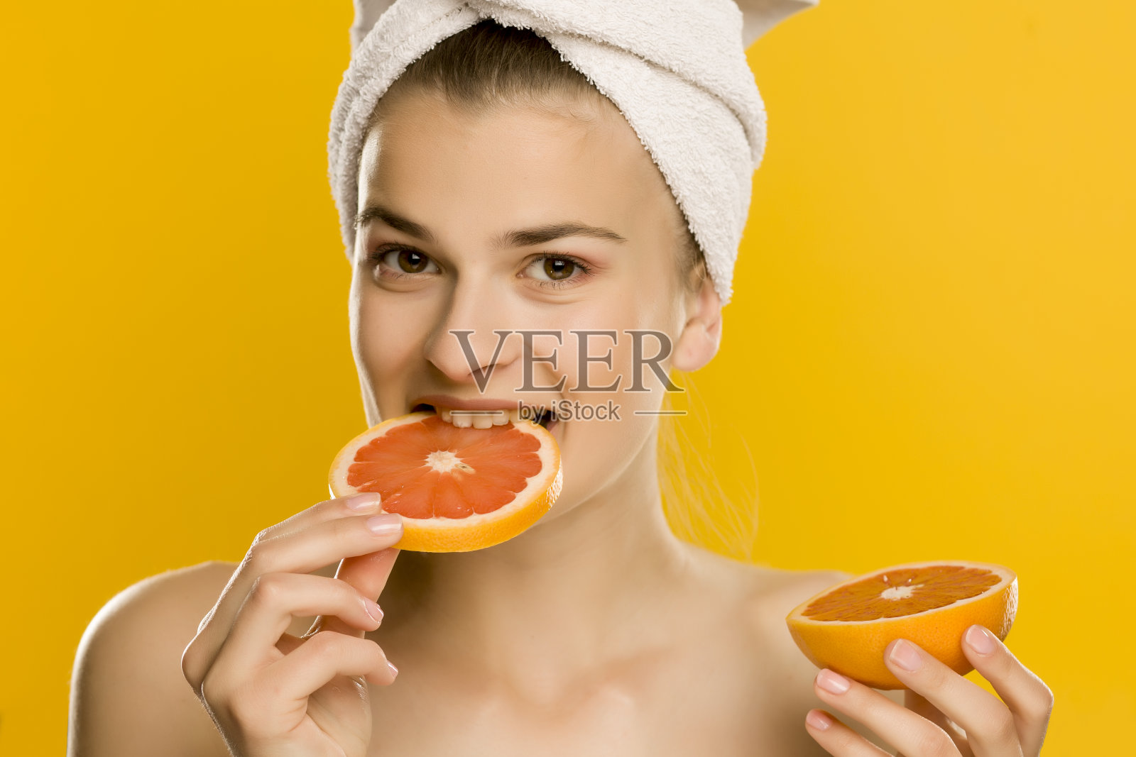 一个年轻美丽的女人在黄色的背景下吃一个红色的葡萄柚的肖像照片摄影图片