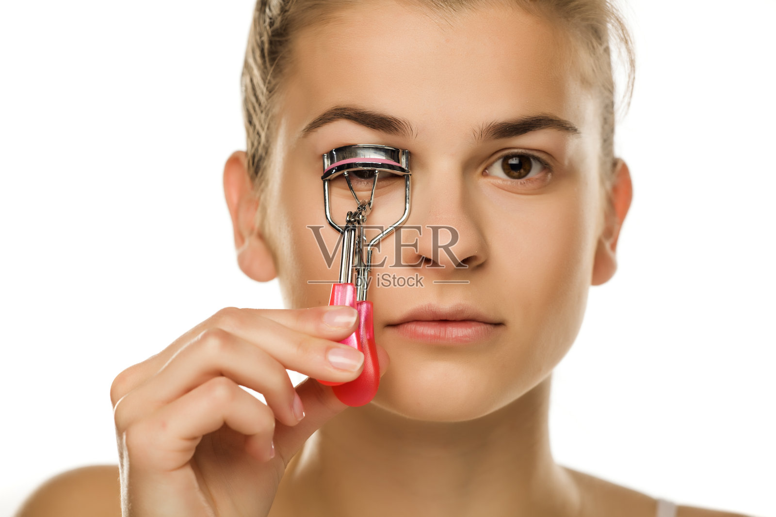 在白色背景上用卷发器卷睫毛的年轻女子照片摄影图片