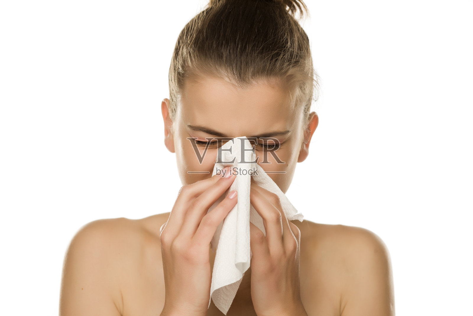 一个年轻女子在白色背景下对着纸巾打喷嚏照片摄影图片