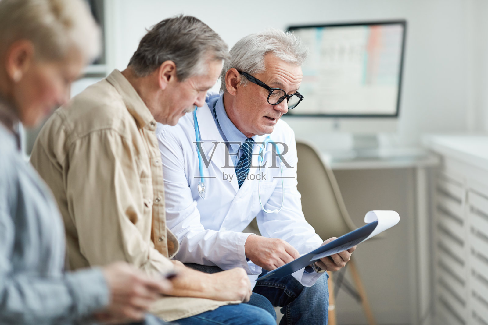 戴眼镜的资深男医生拿着带纸的剪贴板，一边与成熟的病人交谈，一边评论测试结果照片摄影图片