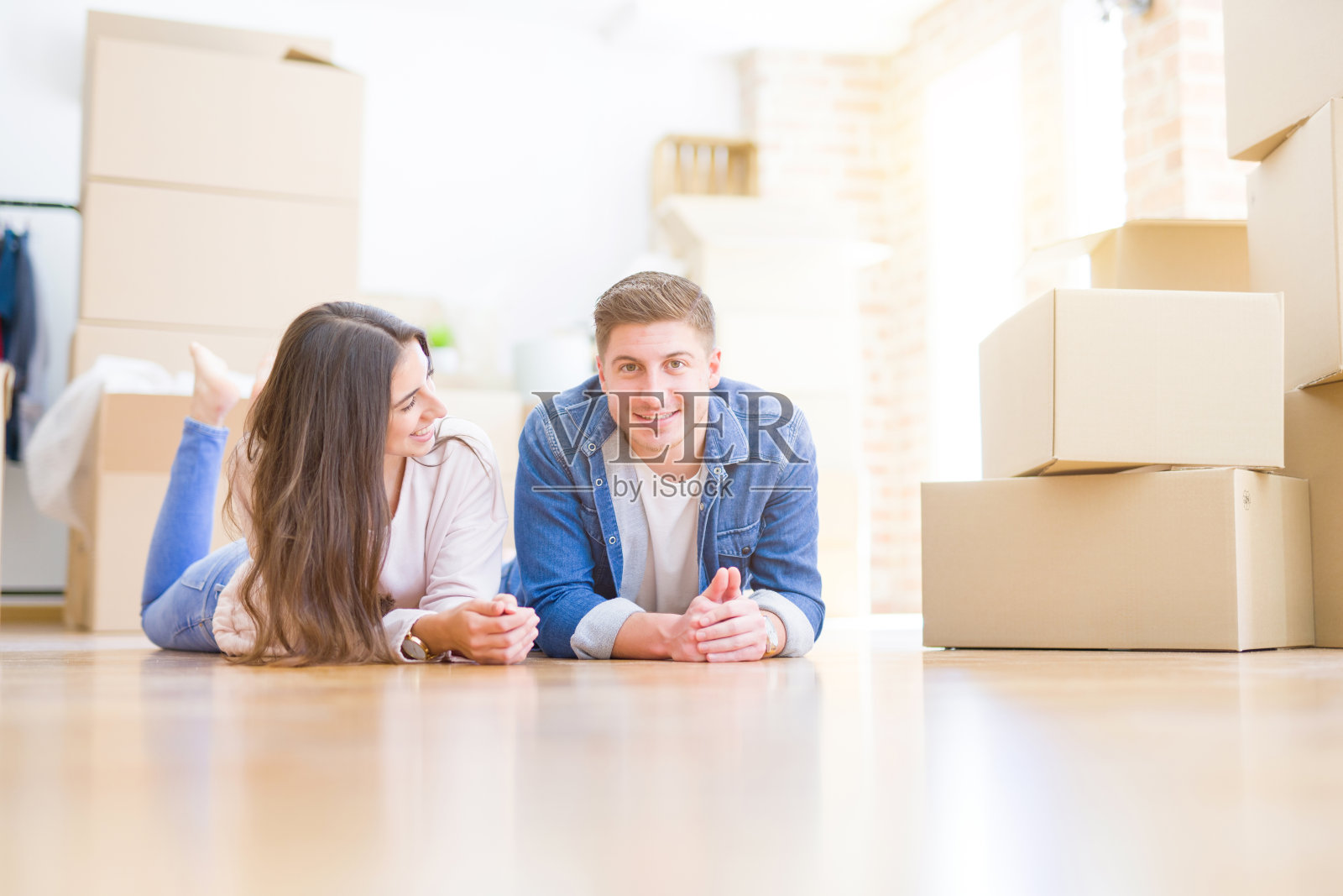 年轻漂亮的夫妇轻松地躺在家里的纸箱周围的地板上，微笑着幸福地搬到一个新房子照片摄影图片