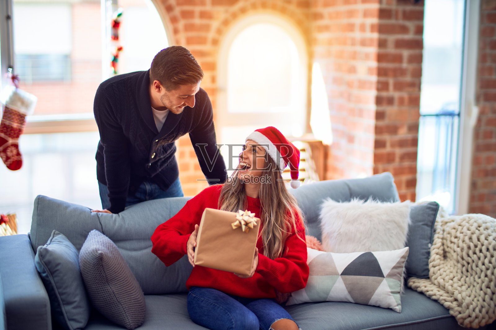 年轻美丽的夫妇微笑着，快乐而自信。男人在家里的圣诞树周围用礼物给女人一个惊喜照片摄影图片
