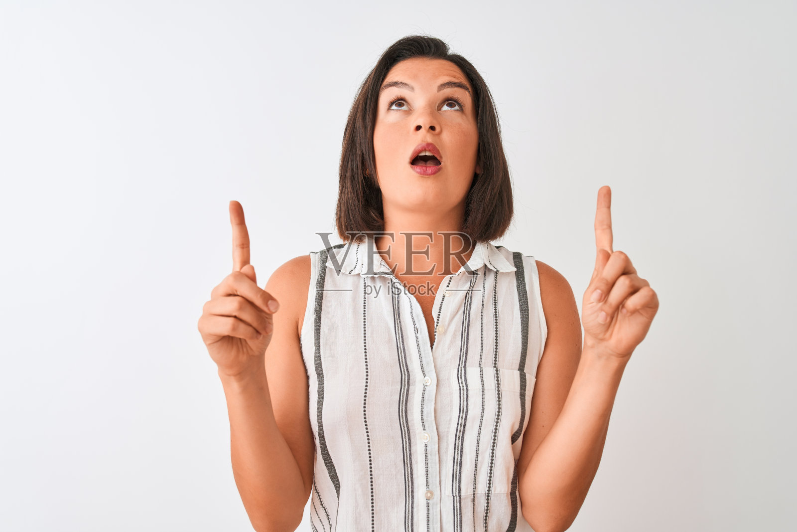 年轻美丽的女人穿着休闲条纹衬衫站在孤立的白色背景惊讶和惊讶的看着和指向手指和举起的手臂。照片摄影图片