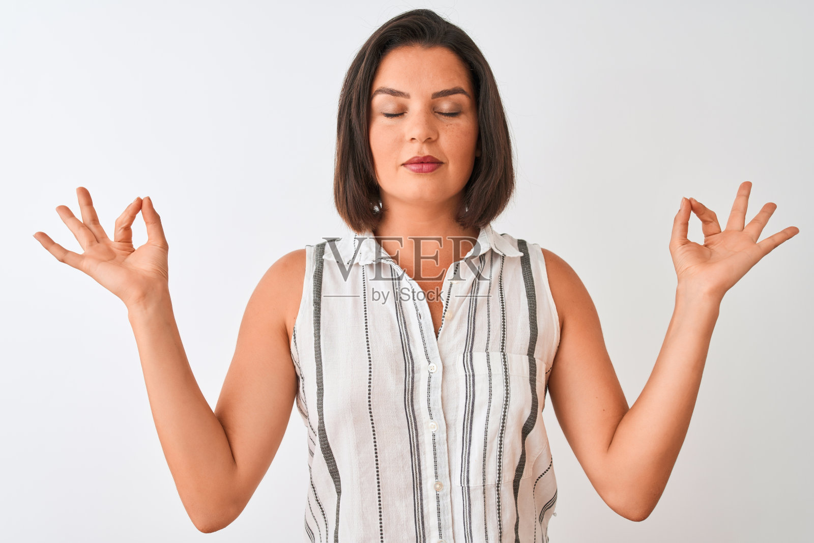 年轻美丽的女人穿着休闲条纹衬衫站在孤立的白色背景放松和微笑，闭上眼睛做冥想手势与手指。瑜伽的概念。照片摄影图片