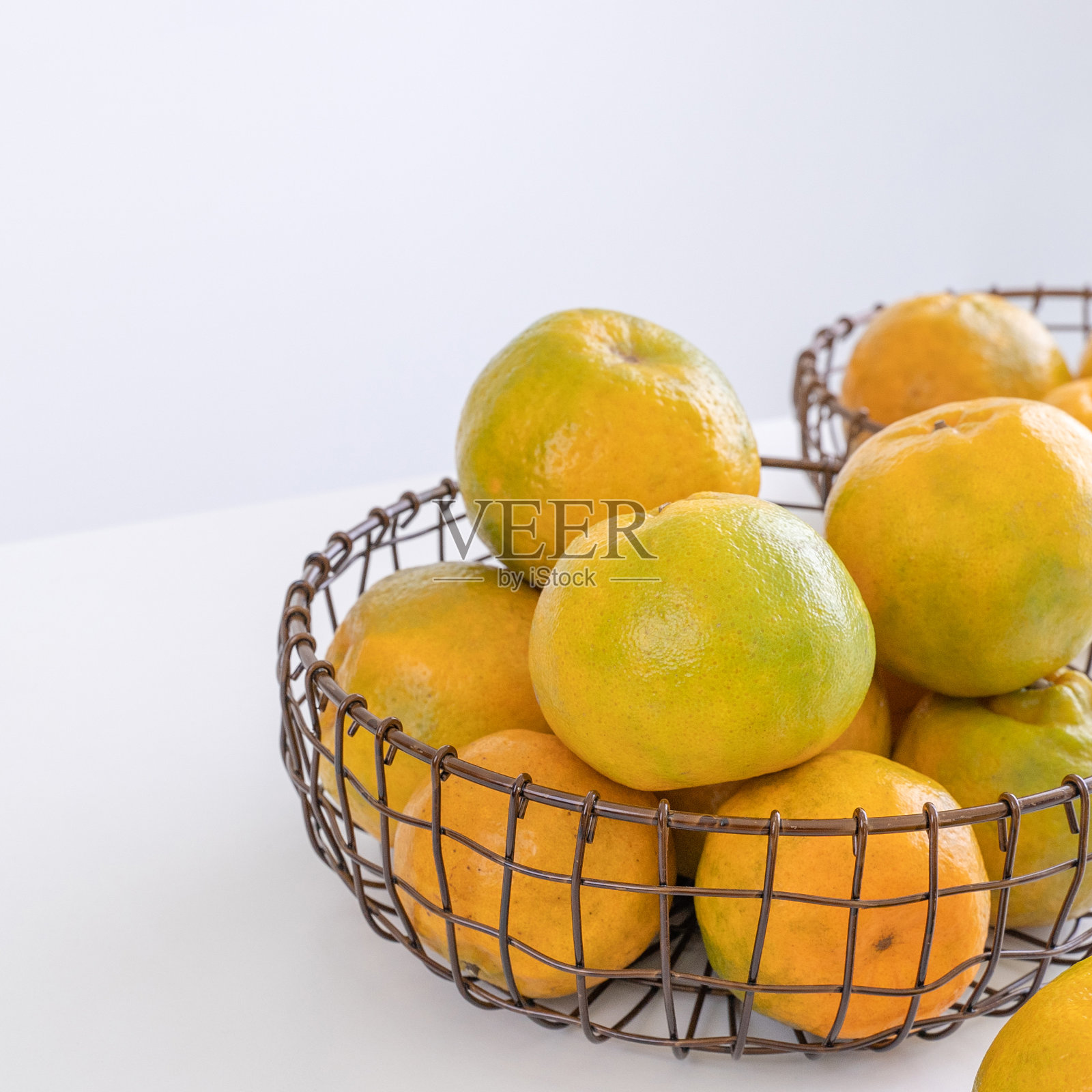 美丽的剥了皮的橘子放在一个盘子和金属篮子里，孤立地放在明亮的白色干净桌子上，在一个现代的厨房岛。照片摄影图片